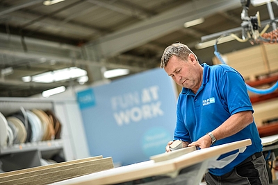 Mann in blauem Shirt schleift eine Holzplatte ©hali GmbH